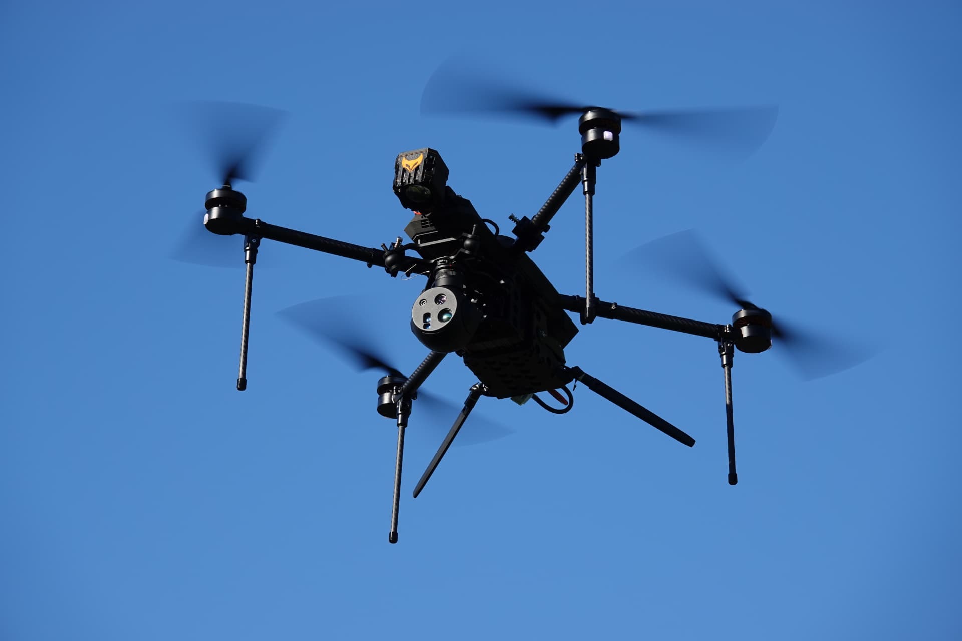 RECCE tactical quadcopter UAV silhouetted against a clear sky